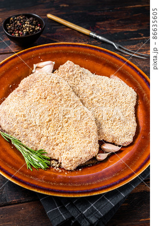 Raw Breaded German Wiener schnitzel on a rustic plate with herbs. Dark wooden background. Top view Raw Breaded German Wiener schnitzel on a rustic plate with herbs. Dark wooden background. Top view 86635605