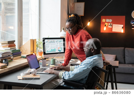 African man with disability working on laptop at the table together with his colleague during their work at home African man with disability working on laptop at the table together with his colleague during their work at home 86636080