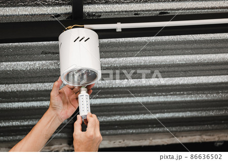 Human hand is installing an LED light bulb in a circular ceiling lamp. 86636502