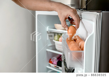 Human hands put chicken eggs in the egg-laying compartment in the refrigerator. 86636505