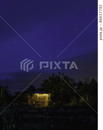 Star tracks over garden and gazebo illuminated with light bulbs. Long exposure of starry night sky. 86637792