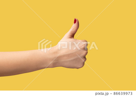 Profile side view closeup of woman hand showing like or thumbs up, approved, positive feedback. Indoor studio shot isolated on yellow background. 86639973