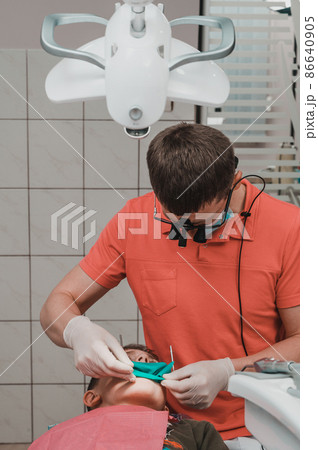 The dentist installs a rubber dam and a clamp for the treatment of a diseased tooth. The dentist installs a rubber dam and a clamp for the treatment of a diseased tooth. 86640905