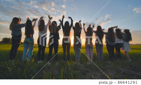 Silhouette of friends of 11 girls waving their hands at sunset in the field. 86641291