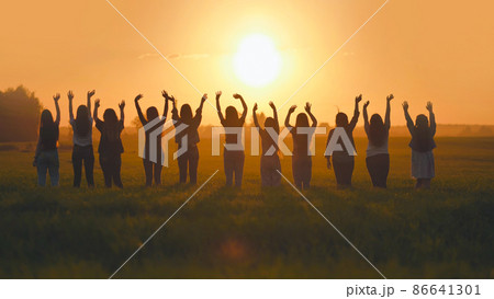 Silhouette of friends of 11 girls waving their hands at sunset in the field. 86641301