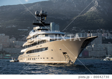 The huge yacht is beige color in sea at sunset, glossy board of the motor boat, the chrome plated handrail, megayacht is moored in sea, sun reflection on glossy board, mountains are on background 86642730