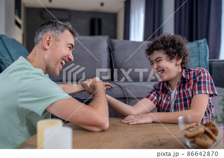 Cheerful man and boy competing in arm wrestling Cheerful man and boy competing in arm wrestling 86642870