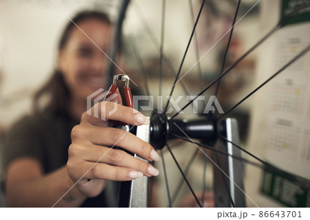 Were focused on quality rather than speed. Shot of an unrecognizable woman standing alone in her shop and repairing a bicycle wheel. 86643701