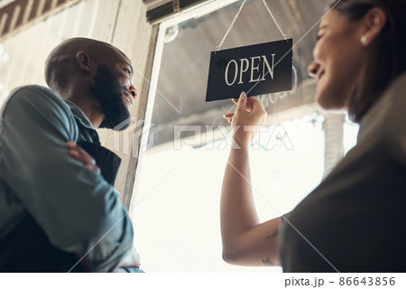Ok turn it, Im ready. Low angle shot of two young colleagues standing together and turning the sign on the door to their bicycle shop. 86643856