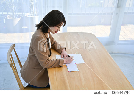 部屋の机でエアメールの封筒に住所を書く女性 部屋の机でエアメールの封筒に住所を書く女性 86644790