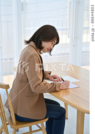 部屋の机でエアメールの封筒に住所を書く女性 86644803