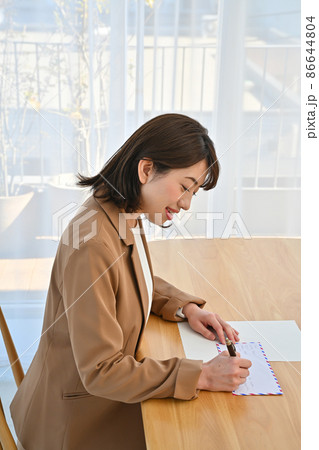 部屋の机でエアメールの封筒に住所を書く女性 部屋の机でエアメールの封筒に住所を書く女性 86644804