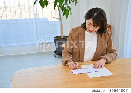 部屋の机でエアメールの封筒に住所を書く女性 86644807
