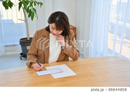 部屋の机でエアメールの封筒に住所を書く女性 86644808