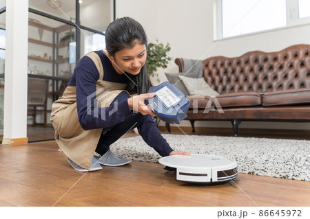 ロボット掃除機のダストボックスを外してごみ捨てをしている若い女性 86645972
