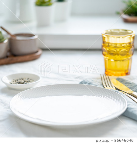 Side view of clean empty white plate, glass of water, fork and knife on white tablecloth 86646046