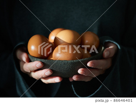 Unusual Easter on dark background. Bowl of brown eggs with hands. 86646401