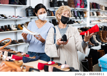 Woman sales consultant in a mask helps a mature woman buyer choose ballet flats 86648811