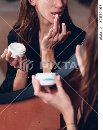 Woman applies a nourishing balm to her lips, moisturizing her skin. Woman applies a nourishing balm to her lips, moisturizing her skin. 86650468
