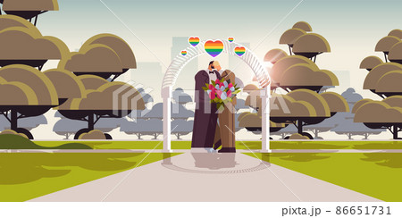 newlywed gay couple with flowers kissing near wedding arch transgender love LGBT community wedding celebration newlywed gay couple with flowers kissing near wedding arch transgender love LGBT community wedding celebration 86651731