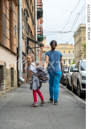 Little Girl Shows her Tongue while Walking with Mom on a Street. Child Indulges and Pranks Little Girl Shows her Tongue while Walking with Mom on a Street. Child Indulges and Pranks 86653154