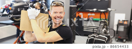 Happy male repairman holding clipboard with documents near motorcycle in car repair shop Happy male repairman holding clipboard with documents near motorcycle in car repair shop 86654433
