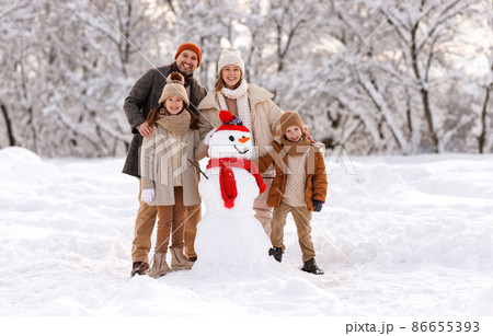 Happy family in warm clothes laughing merrily while making snowman together Happy family in warm clothes laughing merrily while making snowman together 86655393