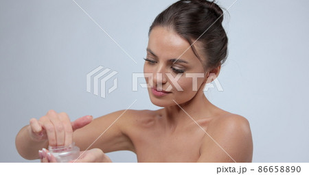 Young caucasian woman applying moisturizing cream on her bare shoulder, bodycare procedures concept. Beauty concept. Young caucasian woman applying moisturizing cream on her bare shoulder, bodycare procedures concept. Beauty concept. 86658890