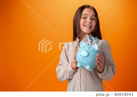 Teen girl with piggy bank on orange color background. Teen girl with piggy bank on orange color background. 86659043