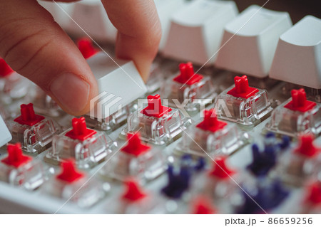 fingers placing a keycap on a white mechanical keyboard 86659256