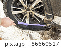 Cleaning a dirty car wheel with a brush scraper from dirt and snow on a sunny frosty winter morning. 86660517