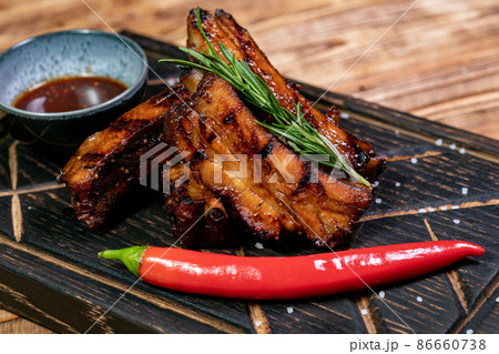 Spicy hot grilled spare ribs from a summer BBQ served with a hot chili pepper and fresh tomatoes on an old vintage wooden cutting board. 86660738