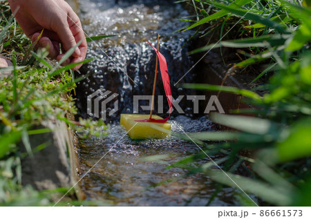 A man lowers a child's boat into a narrow canal or stream.  86661573