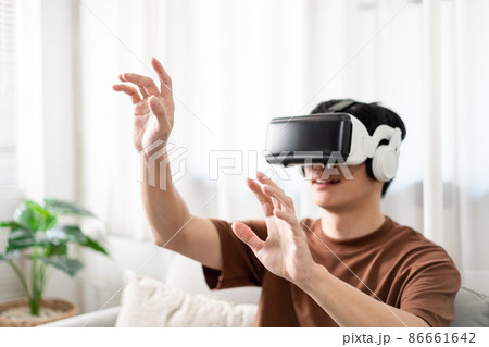 Technology Concept The man with his brown T-shirt and light blue jeans wearing a virtual reality headset while sitting on the sofa 86661642