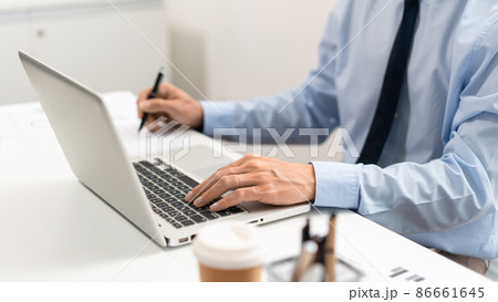 Working Man Conept The male officer sitting in the office, laying his left hand on the laptop, and writing something on the paper with his right hand 86661645