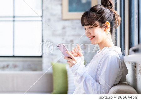 リビングでスマホを見る若い女性 86664458