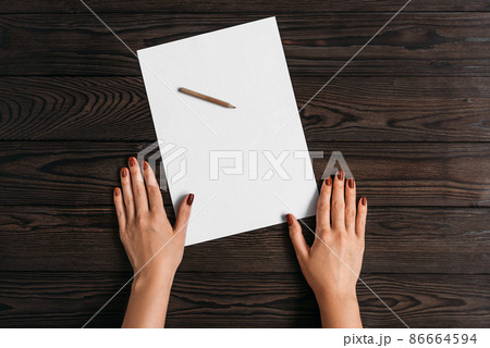 Top view of women's hands, ready to write something on an empty piece of paper lying on a wooden table. White blank sheet of paper with pencil on wooden background. Write a letter on a white sheet Top view of women's hands, ready to write something on an empty piece of paper lying on a wooden table. White blank sheet of paper with pencil on wooden background. Write a letter on a white sheet 86664594