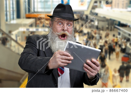 Shocked senior businessman using digital tablet while standing on escalator at airport. Shocked senior businessman using digital tablet while standing on escalator at airport. 86667400