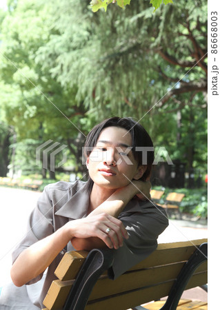 公園でくつろぐカメラ目線の若い男性 86668003