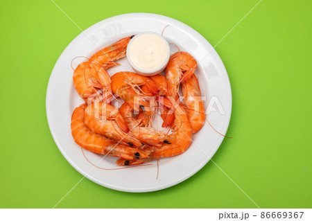 Boiled fresh shrimps with sauce in small bowl on white plate on green 86669367
