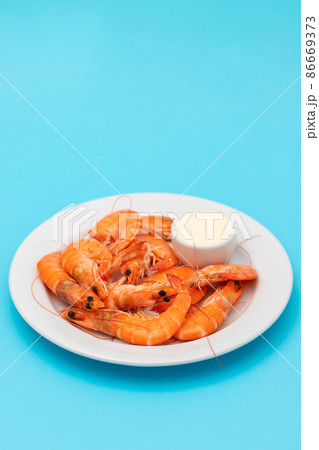 Boiled fresh shrimps with sauce in small bowl on white plate on blue 86669373