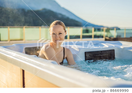 Portrait of young carefree happy smiling woman relaxing at hot tub during enjoying happy traveling moment vacation life against the background of green big mountains 86669990