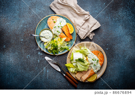 Healthy food meal grilled salmon steaks with dill sauce and salad leafs on two plates Healthy food meal grilled salmon steaks with dill sauce and salad leafs on two plates 86676894