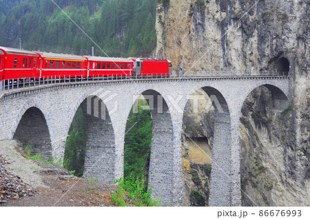Passenger train goes from Chur to St. Moritz on Landwasser viaduct. 86676993