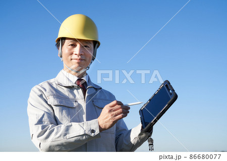 青空のもとでタブレットを手に持つヘルメット着用の男性 86680077