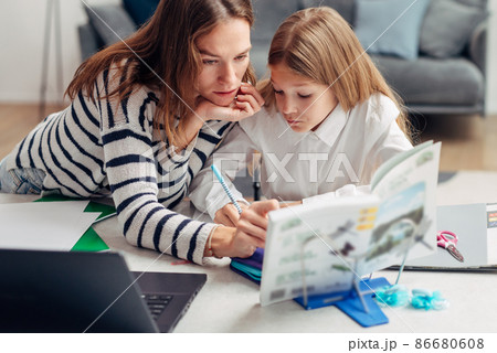 Girl writes in copybook mother looking at textbook. Girl writes in copybook mother looking at textbook. 86680608
