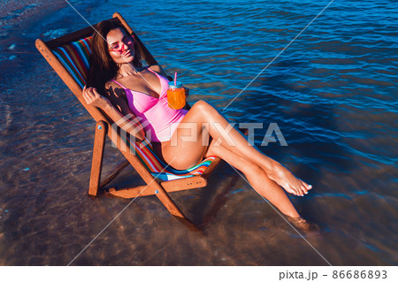 Beautiful sexy girl in a pink bathing suit relaxing on the beach while lying at the deck chair 86686893