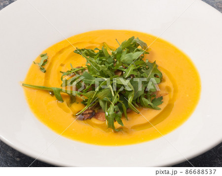 cream of pumpkin soup with arugula on a white plate cream of pumpkin soup with arugula on a white plate 86688537