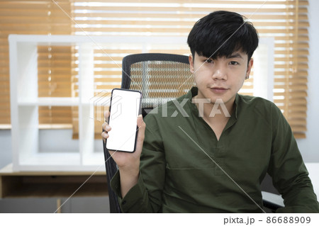 Handsome young asian man holding and showing smart phone with blank screen. Handsome young asian man holding and showing smart phone with blank screen. 86688909