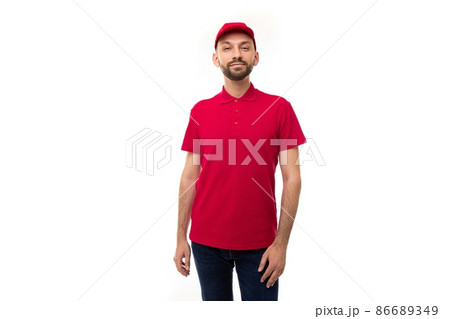 young courier from a delivery service in a red uniform looking at the camera on a white background 86689349